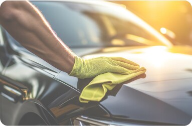 A mobile repair technician wearing a yellow glove polishing the hood of a car to maintain its like-new appearance.