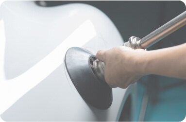 A close-up of a mobile technician repairing an exterior dent on a white car.