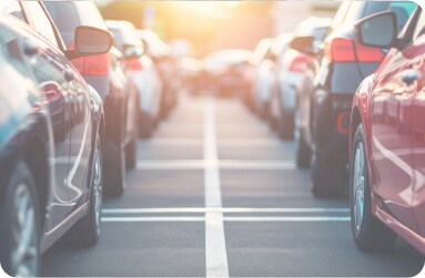 A row of mostly silver and black parked cars lined up neatly in an outdoor parking lot with a focus on rear taillights.